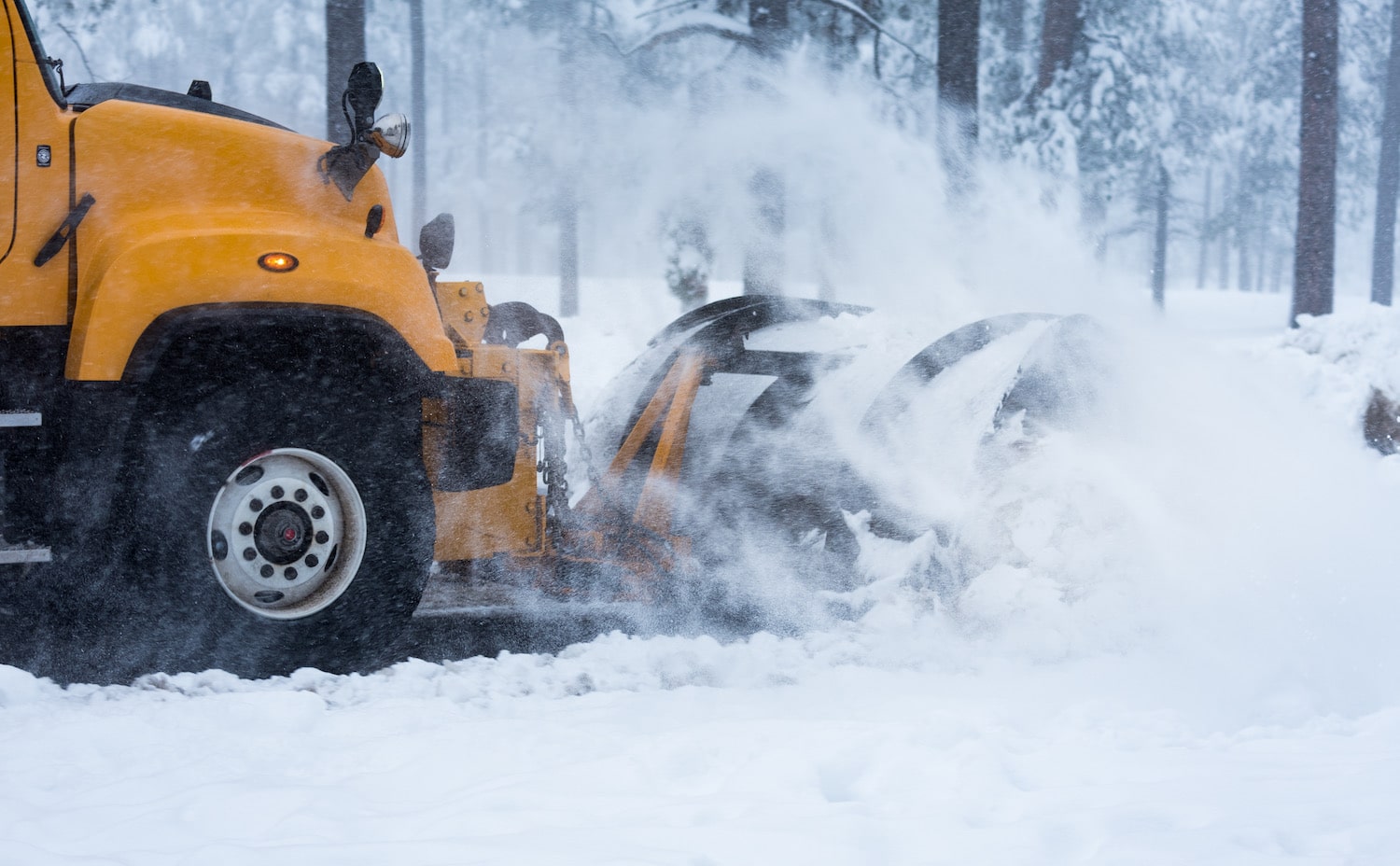 A yellow truck is blowing snow on the road.