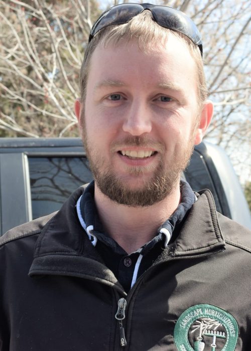 A man in black jacket standing next to truck.